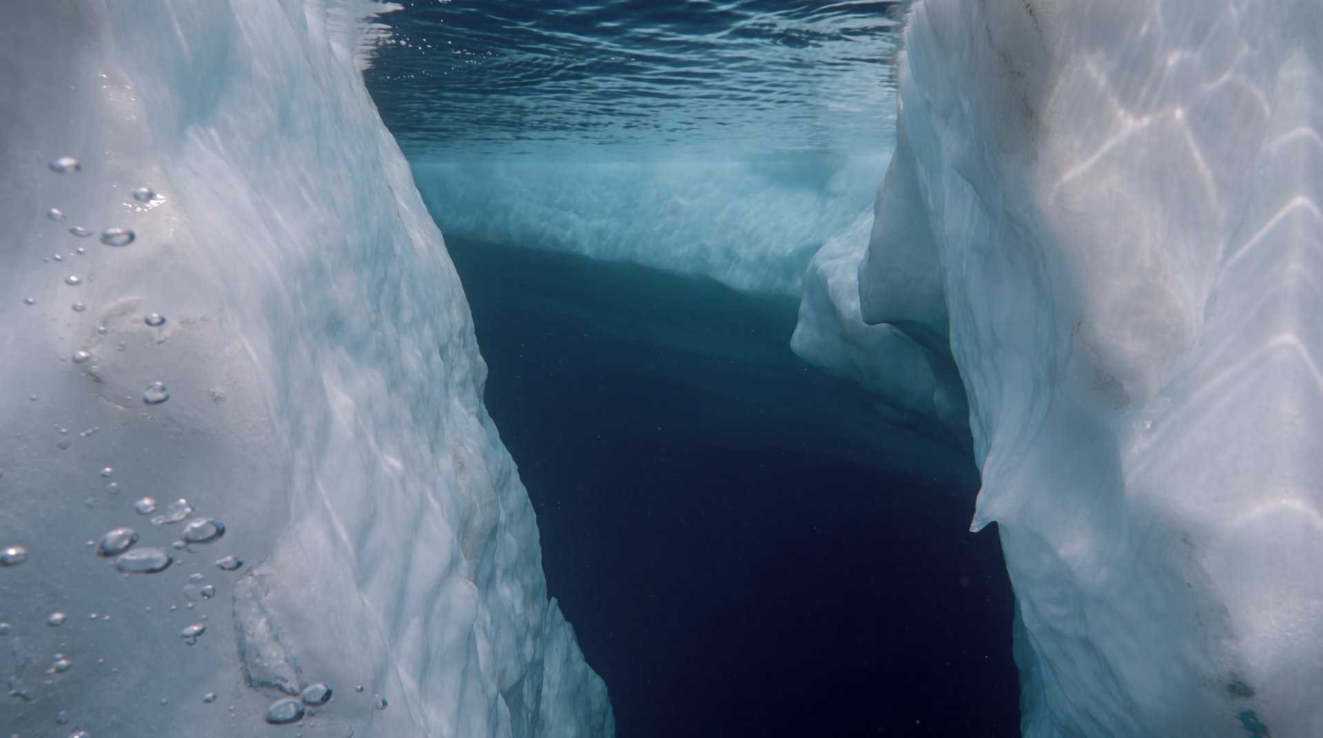 The camera passes below the waterline between two close walls of ice.