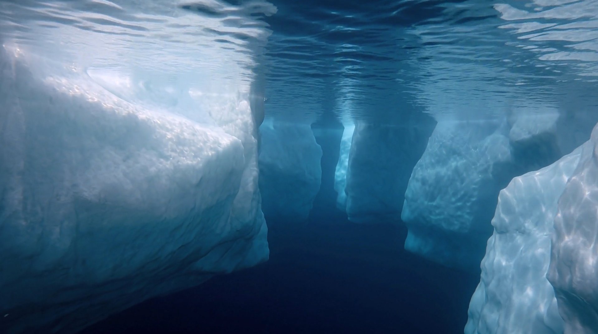 An underwater passage between iceberg walls, with a narrow gap visible in the distance.